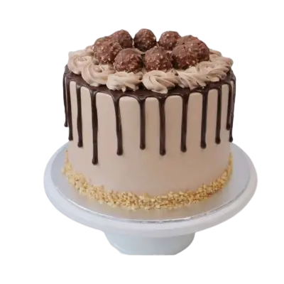 "A round, tan-frosted cake with a dark chocolate drip, topped with light brown buttercream swirls and Ferrero Rocher truffles, with crushed nuts around the base.""A round, tan-frosted cake with a dark chocolate drip, topped with light brown buttercream swirls and Ferrero Rocher truffles, with crushed nuts around the base."